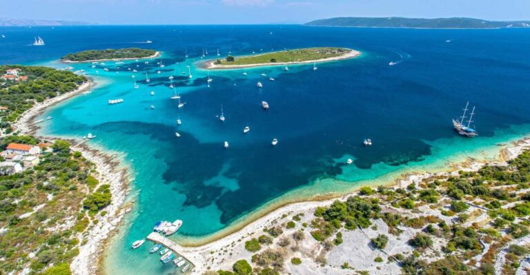 Luftaufnahme einer wunderschönen Küstenregion mit klarem, blauem Wasser, mehreren kleinen Inseln und zahlreichen vor Anker liegenden Booten und Yachten. Grüne Vegetation und felsiges Gelände umgeben die Küste, und auf dem Land sind einige Gebäude zu sehen.