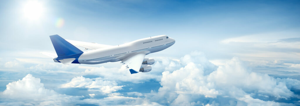 Ein großes Verkehrsflugzeug mit blauem Heck und blauen Flügelspitzen fliegt vor einem klaren, sonnigen Himmel über den Wolken und demonstriert, wie einfach eine Anreise mit dem Flugzeug ist.
